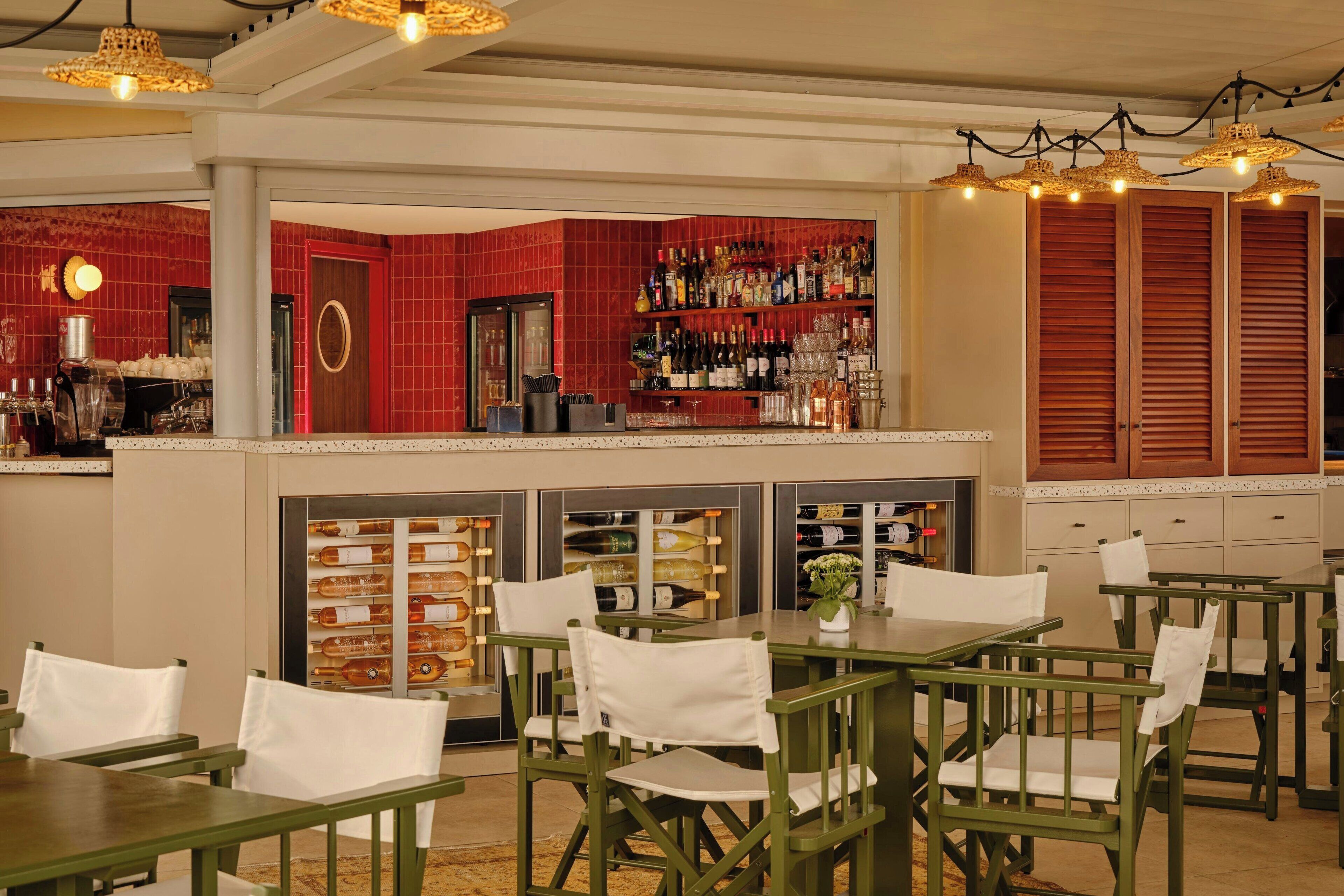 A bar area with green chairs and tables, a wine display, and a red-tiled wall.