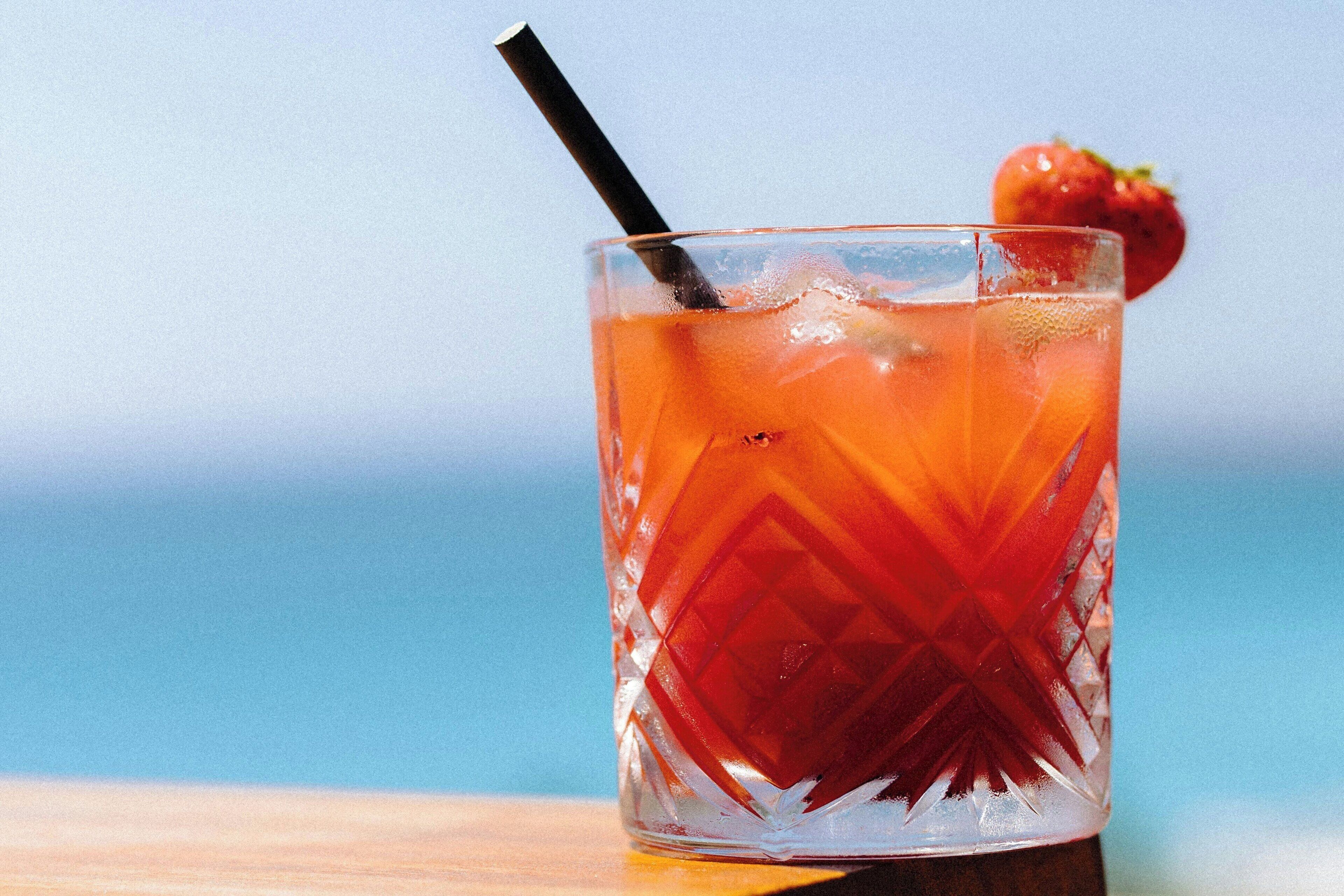 Un verre transparent orné d’un motif en losanges, contenant une boisson rouge, une paille noire et une fraise en guise de décoration.