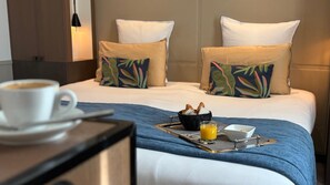 A hotel room with a bed, a bedside table with a cup of coffee, a tray with breakfast items, and a basket of bread. - Villa Saxe Eiffel (Paris)