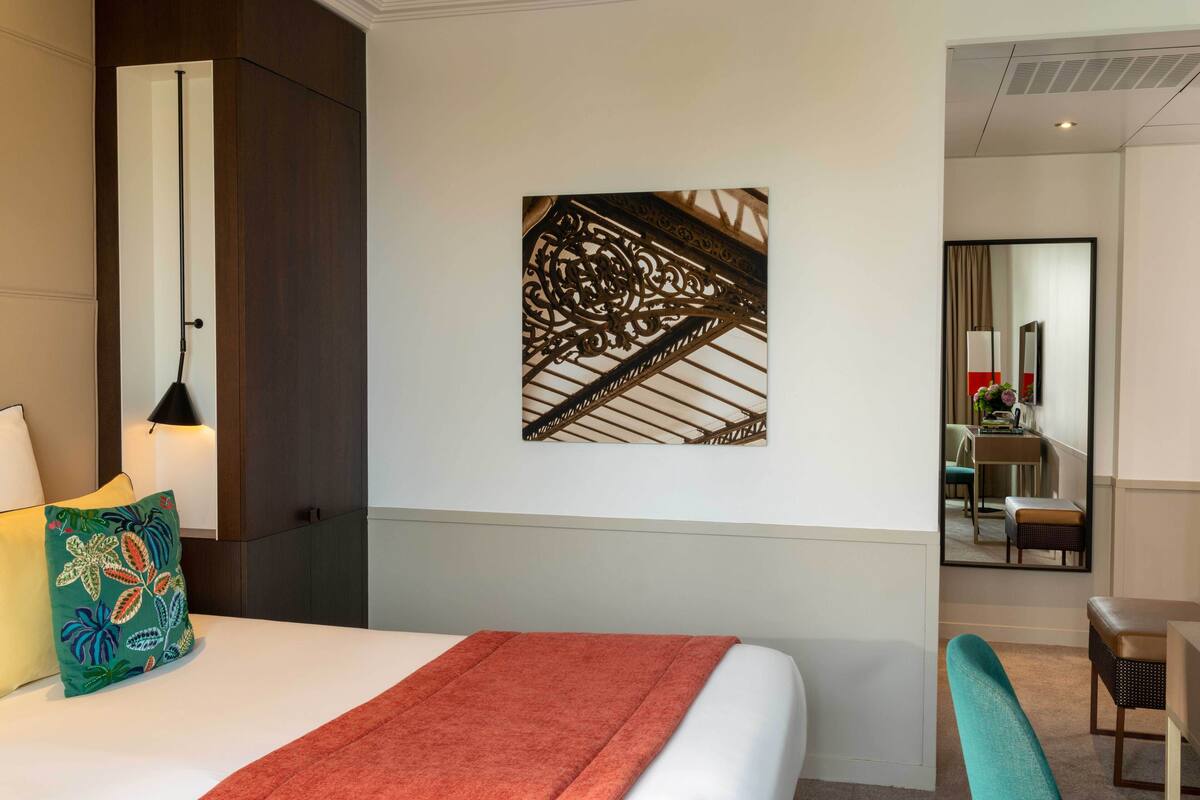 A hotel room with a bed, a wall-mounted artwork, a desk, and a chair.