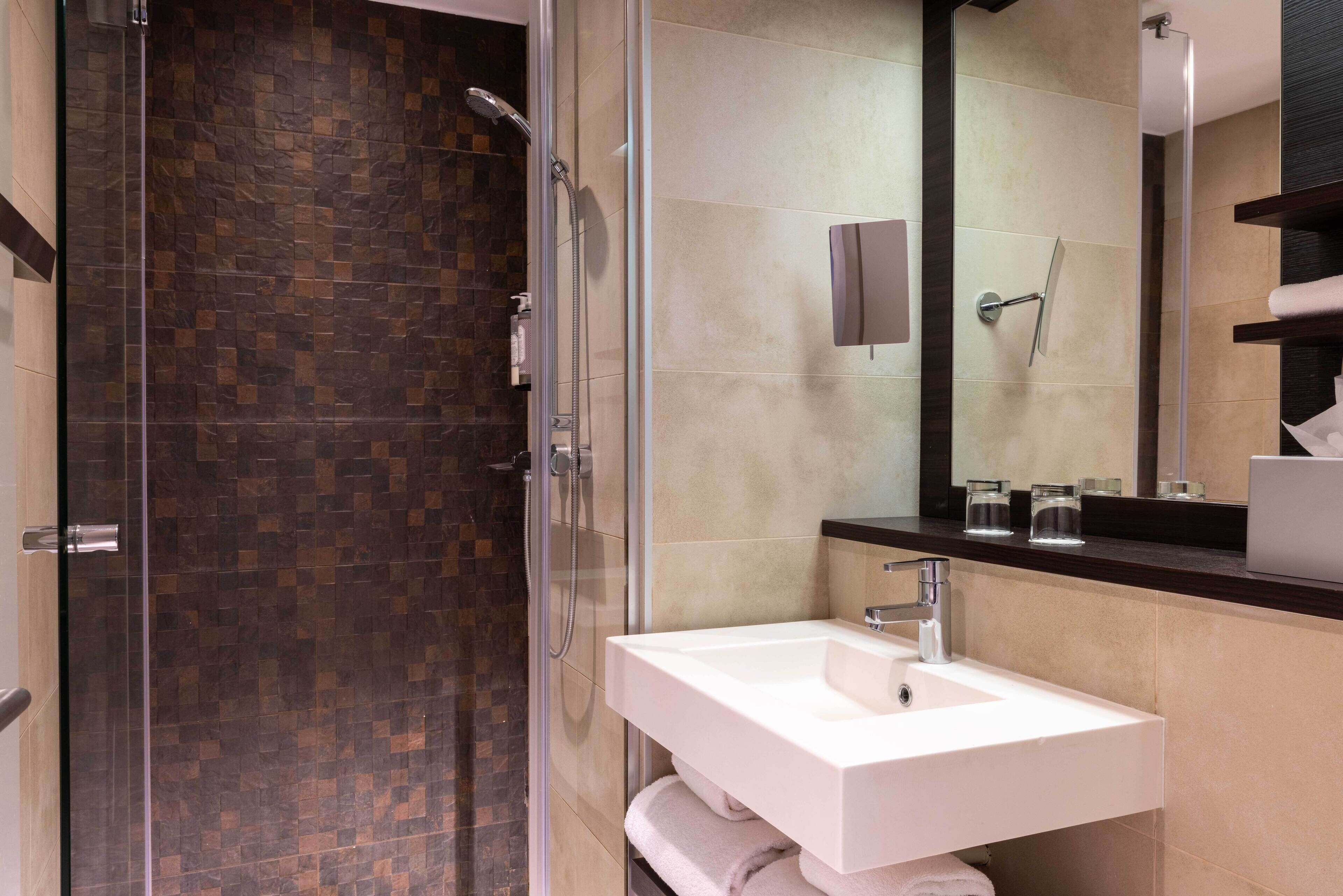 A modern bathroom with a glass-enclosed shower, a white sink, and a large mirror.