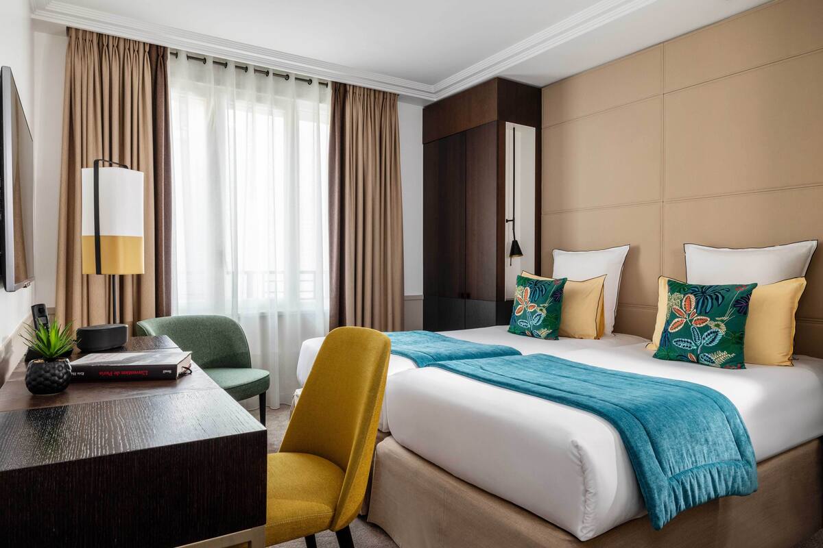 A hotel room with a bed, a desk, a chair, a lamp, and a plant.