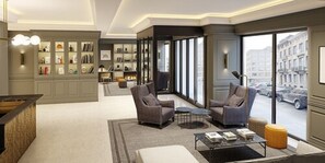 A modern hotel lobby with a seating area, a bookshelf, and a view of the street. - Hotel Avenue Louise Brussels - Trademark Collection by Wyndham (Brussels)