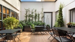 A patio with a table and chairs, surrounded by potted plants and a white wall. - Hotel Avenue Louise Brussels - Trademark Collection by Wyndham (Brussels)