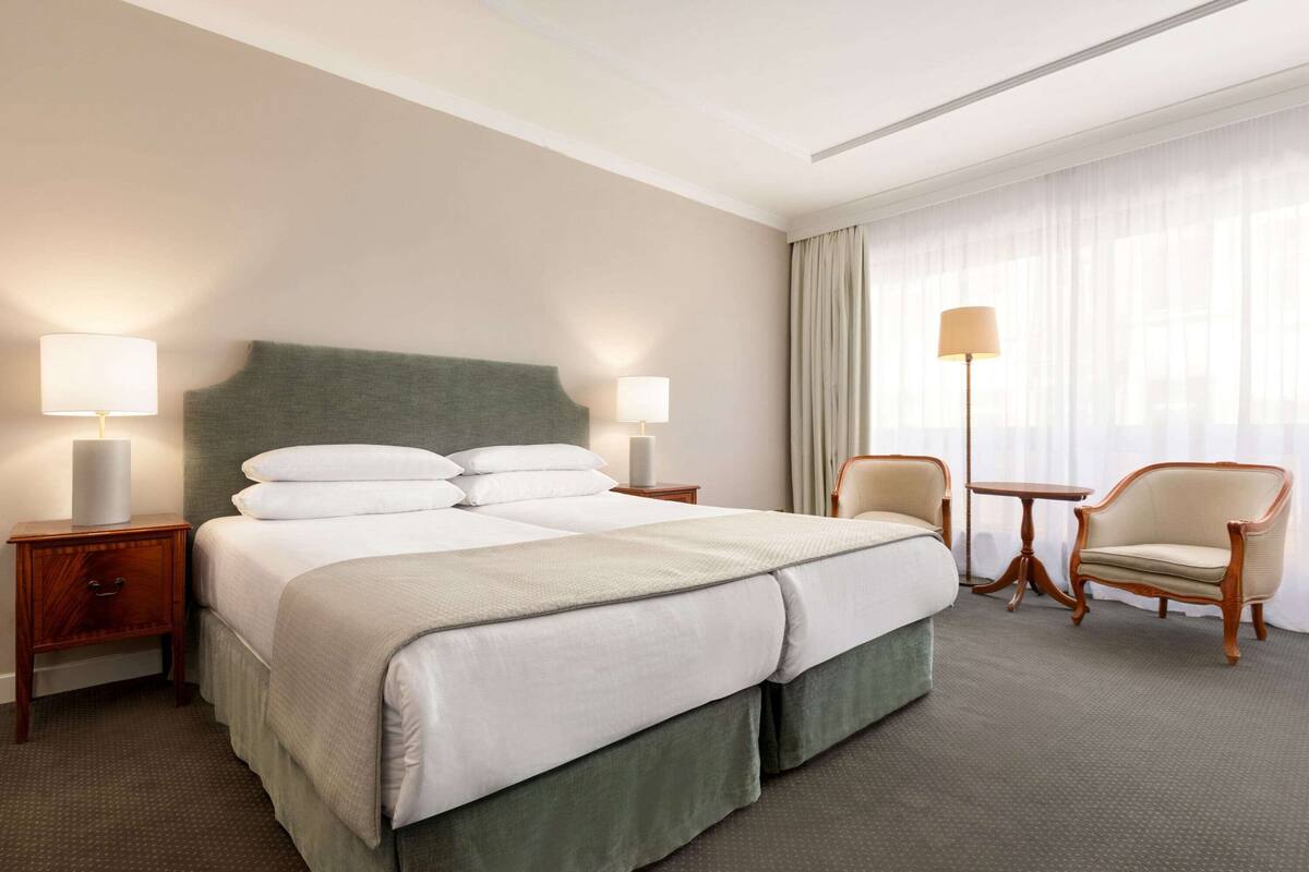 A hotel room with a large bed, two bedside tables, a chair, a small table, and a lamp.