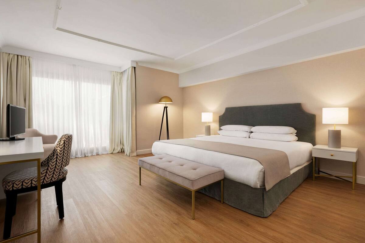 A modern hotel room with a large bed, bedside tables, a desk, and a chair.