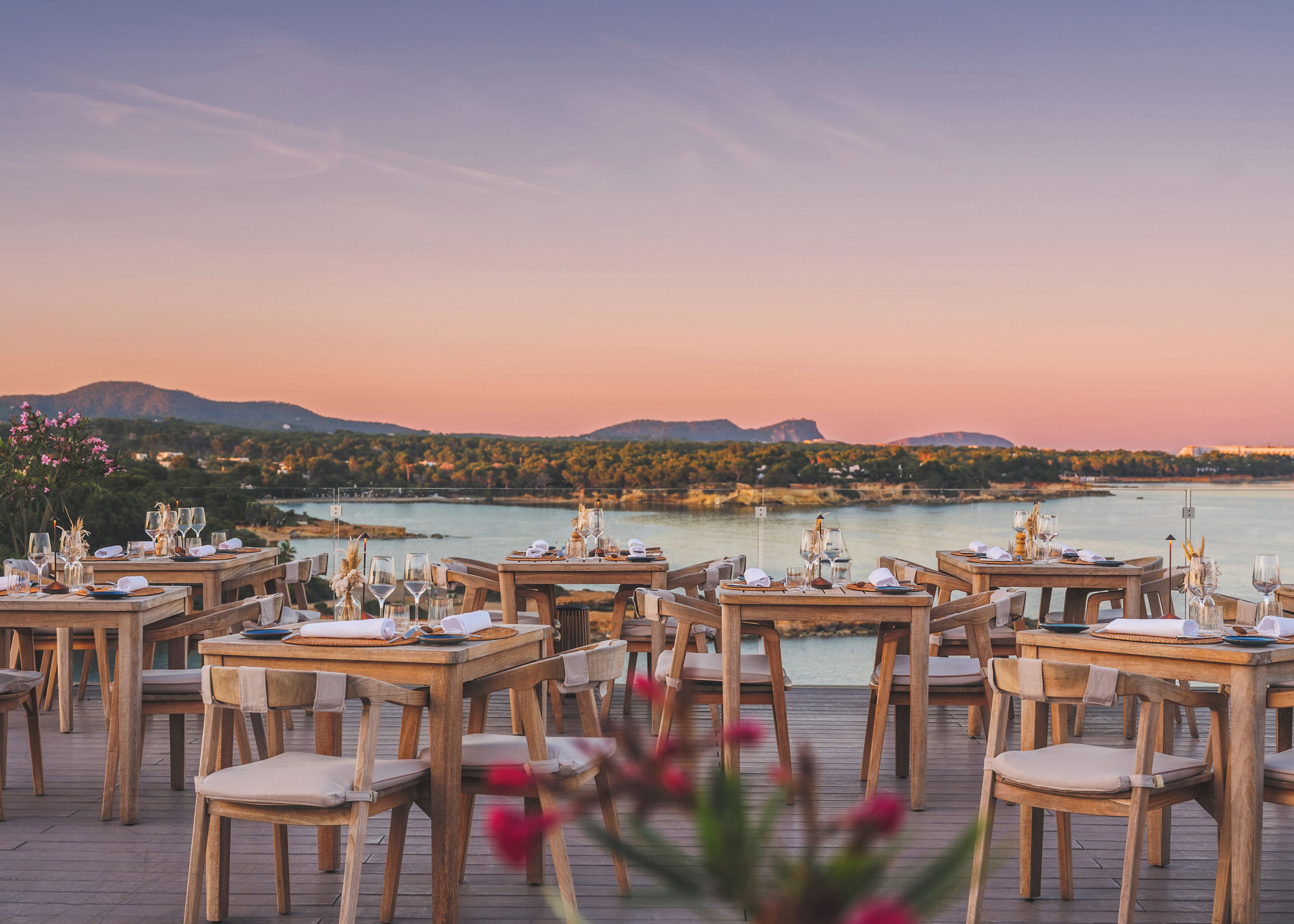 Tables et chaises pour prendre les repas en plein air, disposées devant un plan d’eau et avec vue sur les montagnes.
