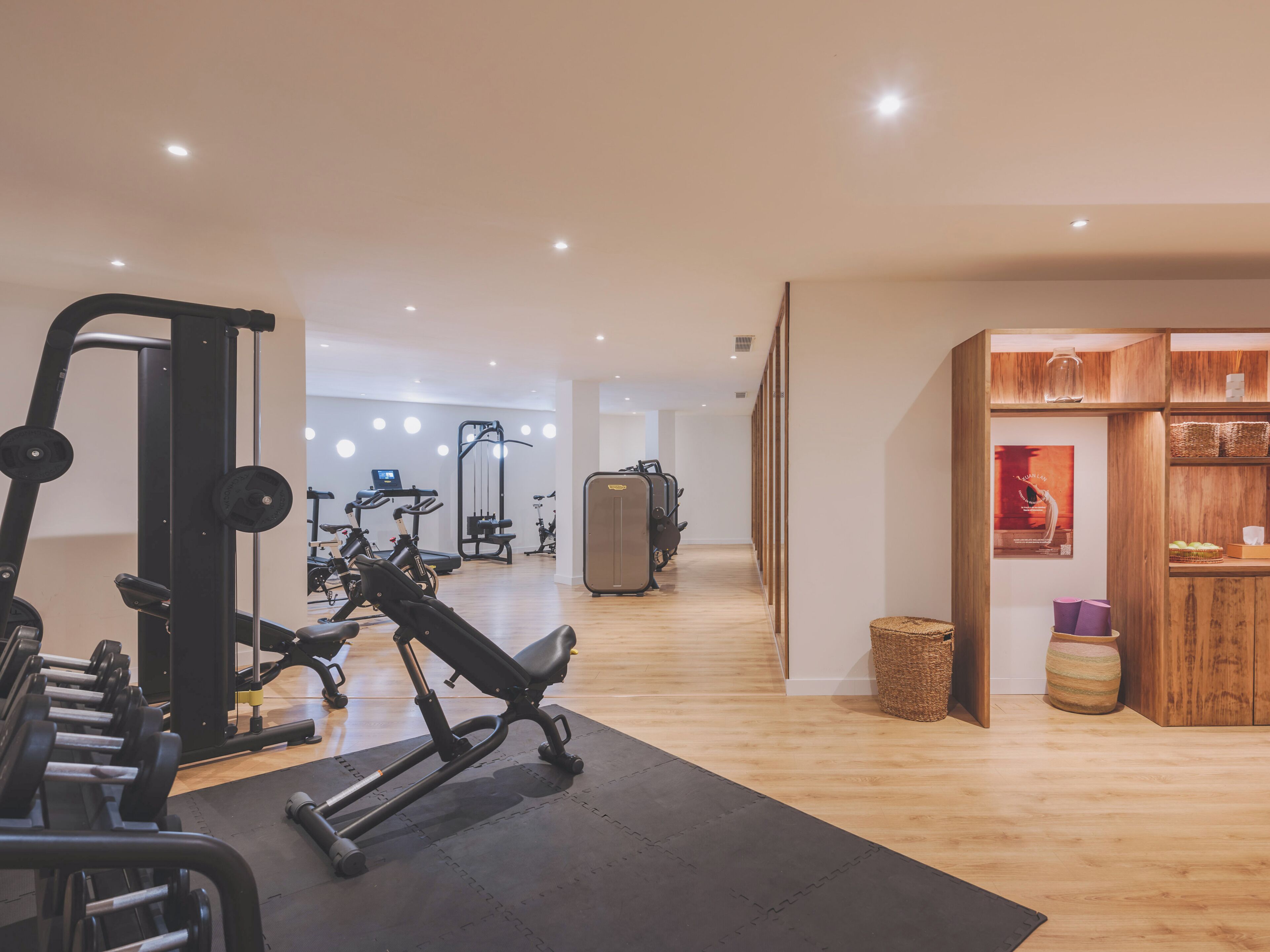 A gym with exercise equipment, a wooden floor, and a wall with baskets and a poster.