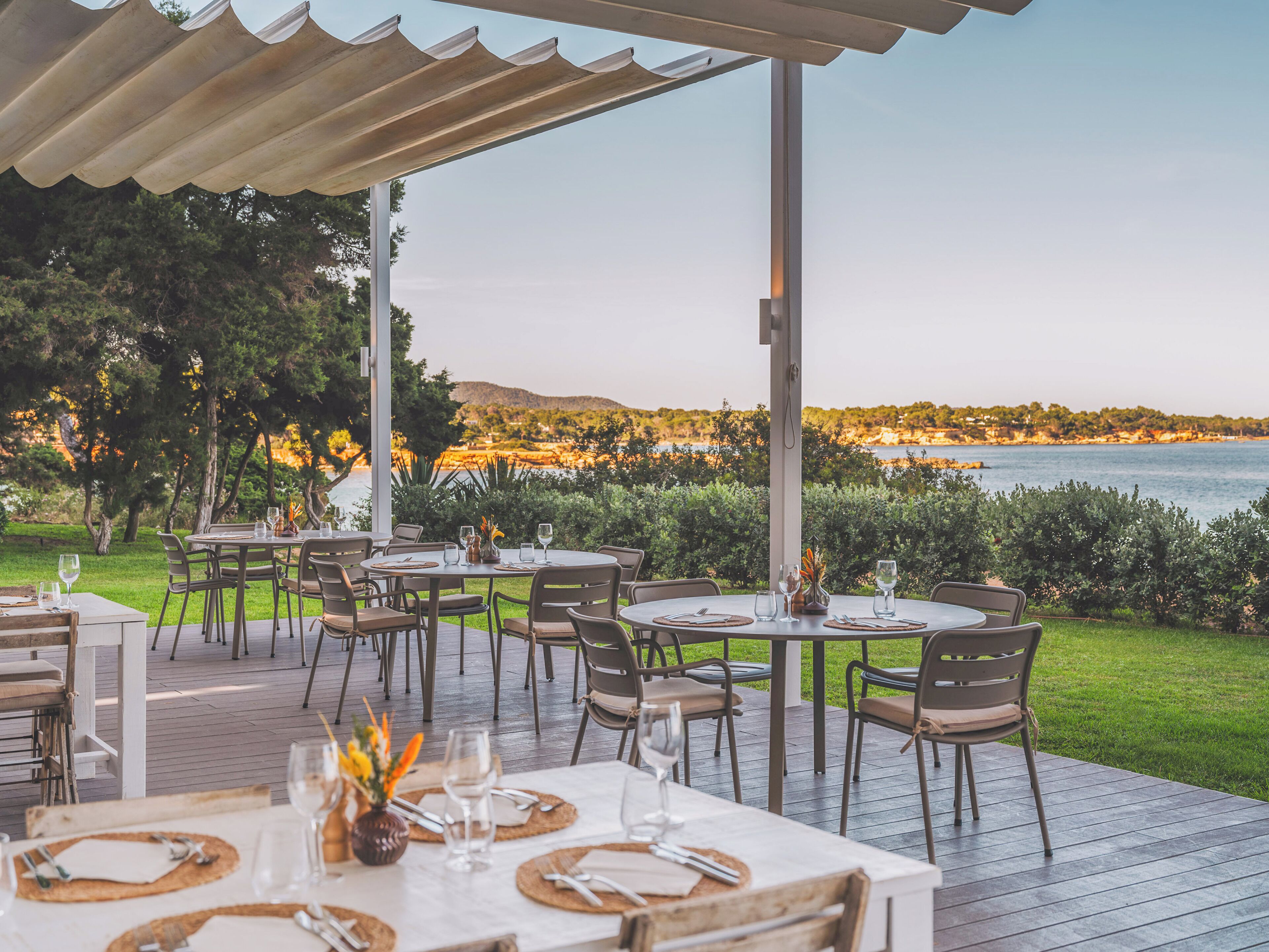 Un espacio de comedor al aire libre con mesas y sillas, con vistas panorámicas del mar y las colinas.