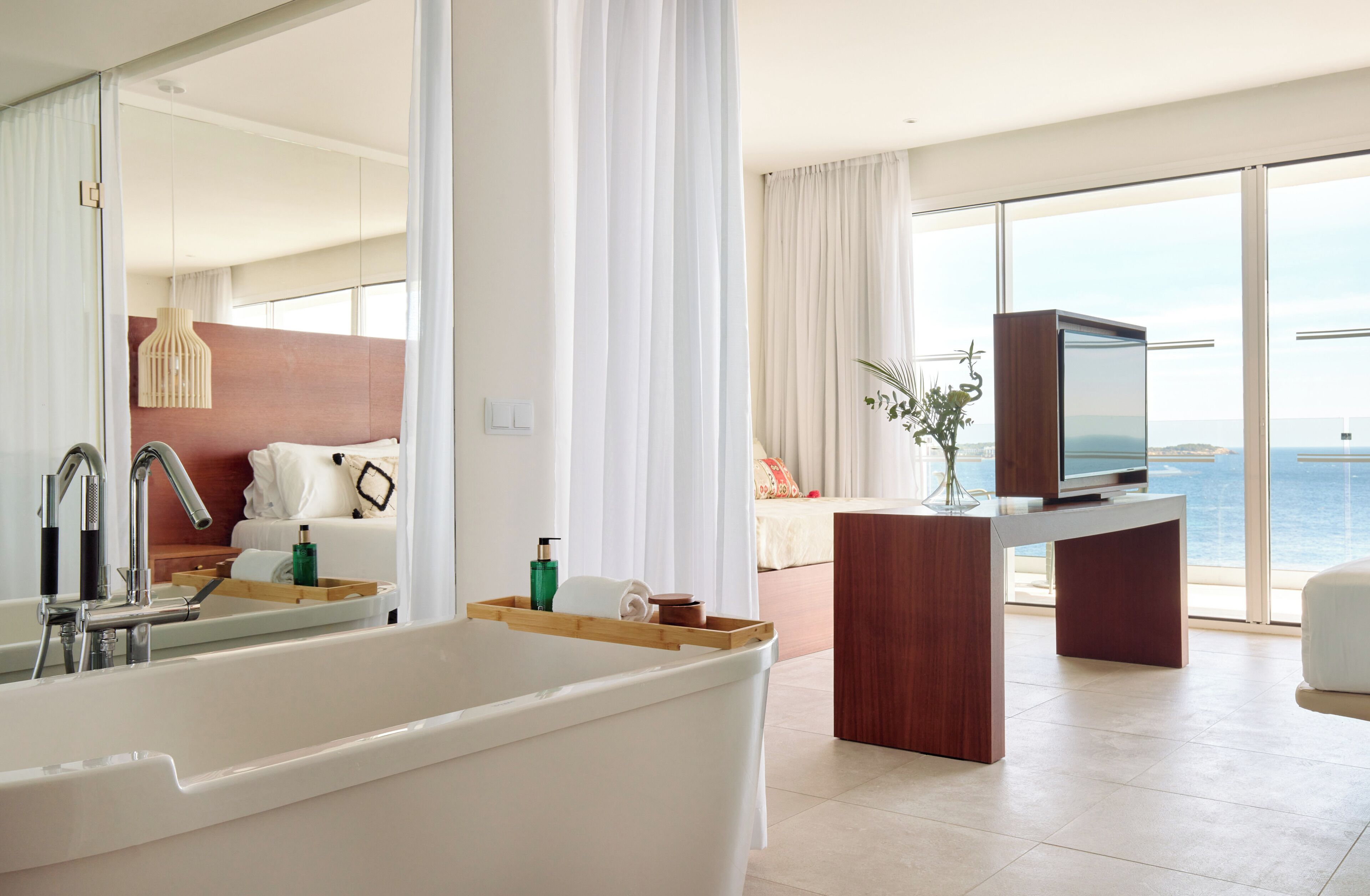 Ein modernes Badezimmer mit einer Badewanne, einem Waschtisch inklusive Spiegel und einem Fernseher auf einem Holzboden.