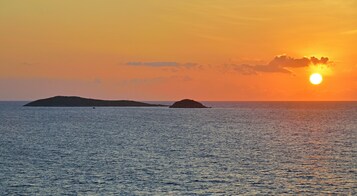 Un atardecer sobre un mar tranquilo con dos islas a lo lejos.