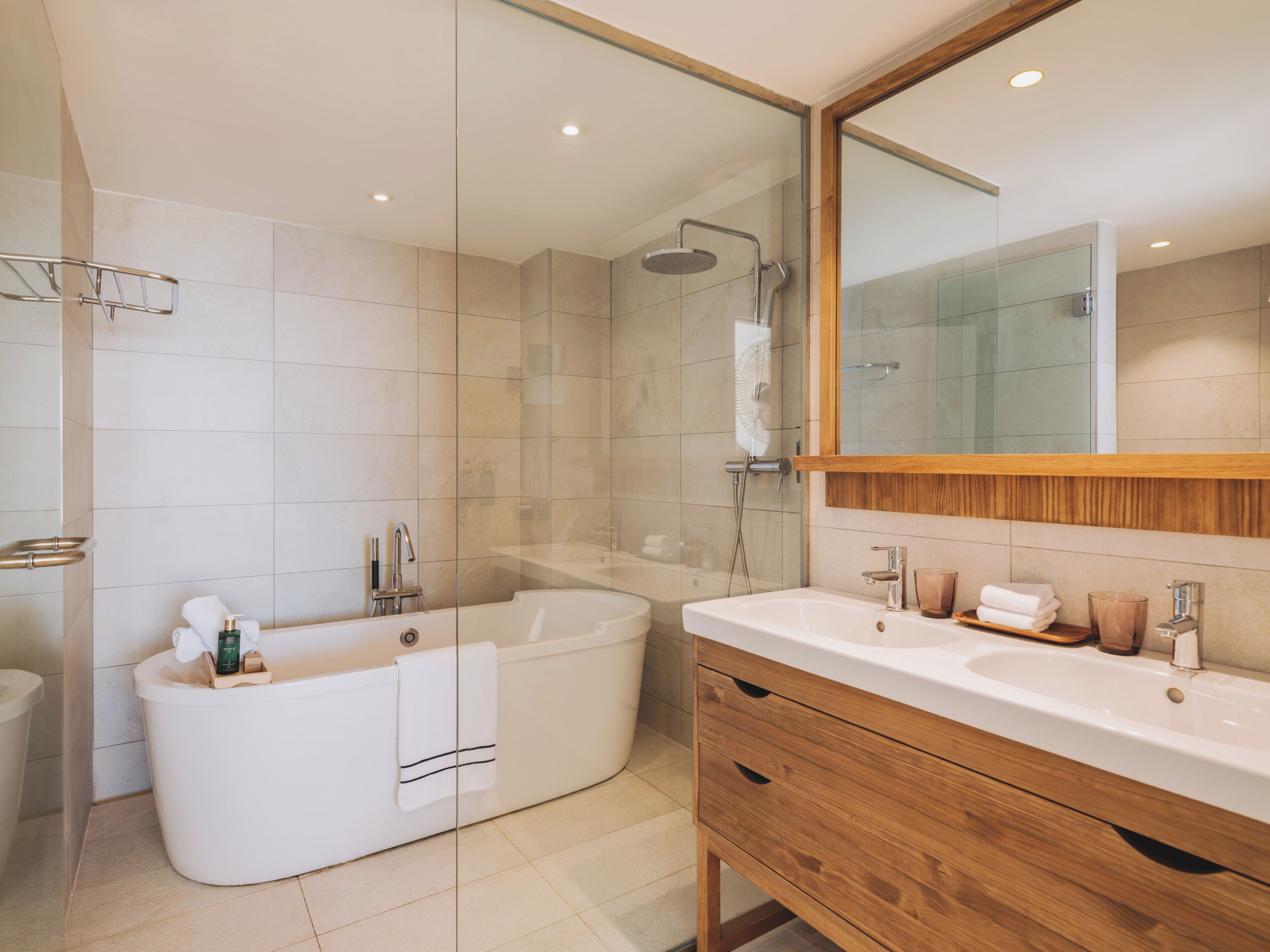 A modern bathroom with a freestanding bathtub, a glass-enclosed shower, and a wooden vanity with a sink and mirror.