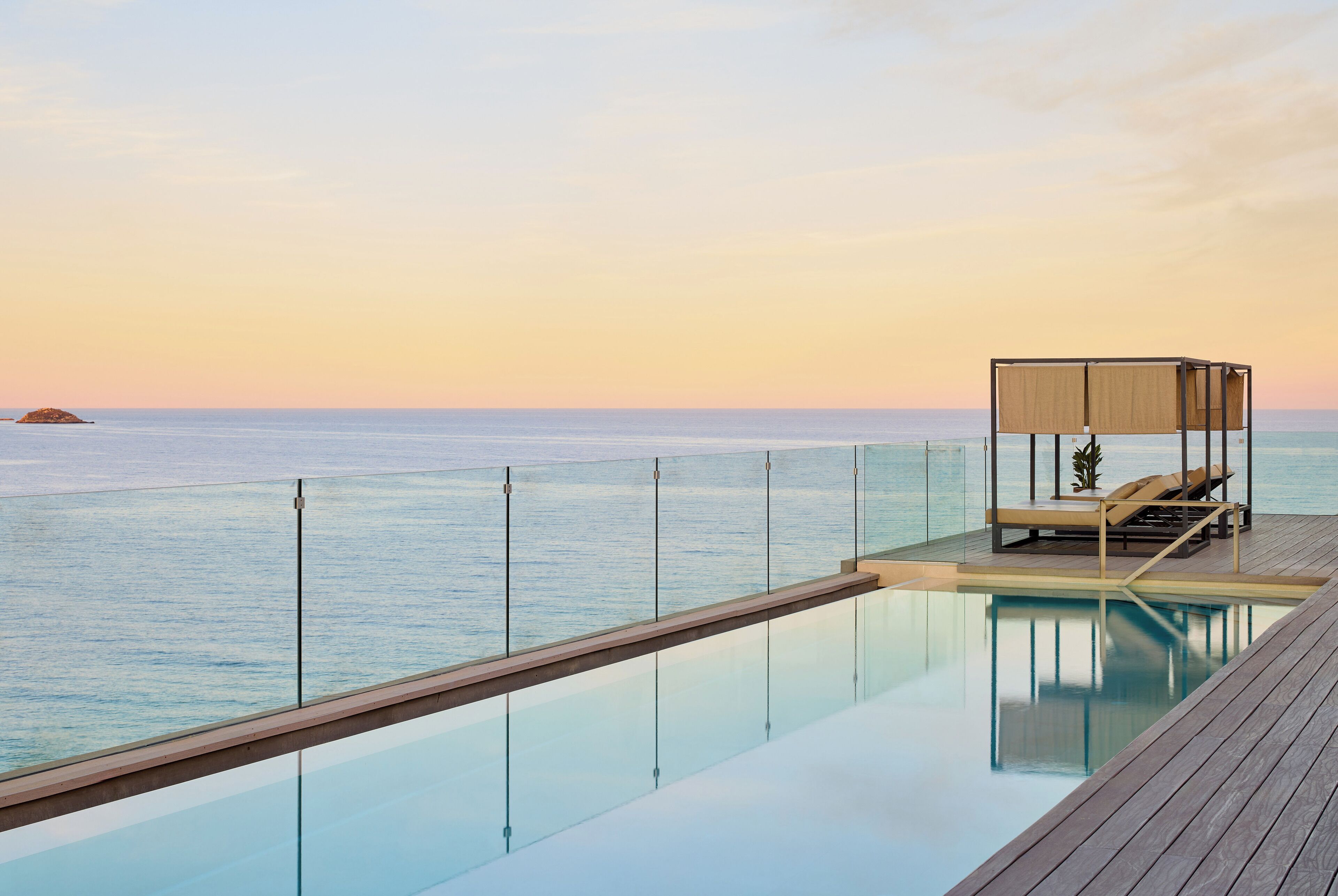 Una piscina sense fi amb un pont de fusta i zona de relaxació amb tolda, amb vista al mar.
