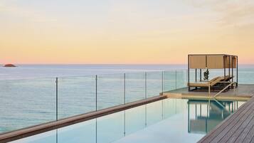 Una piscina sense fi amb un pont de fusta i zona de relaxació amb tolda, amb vista al mar.