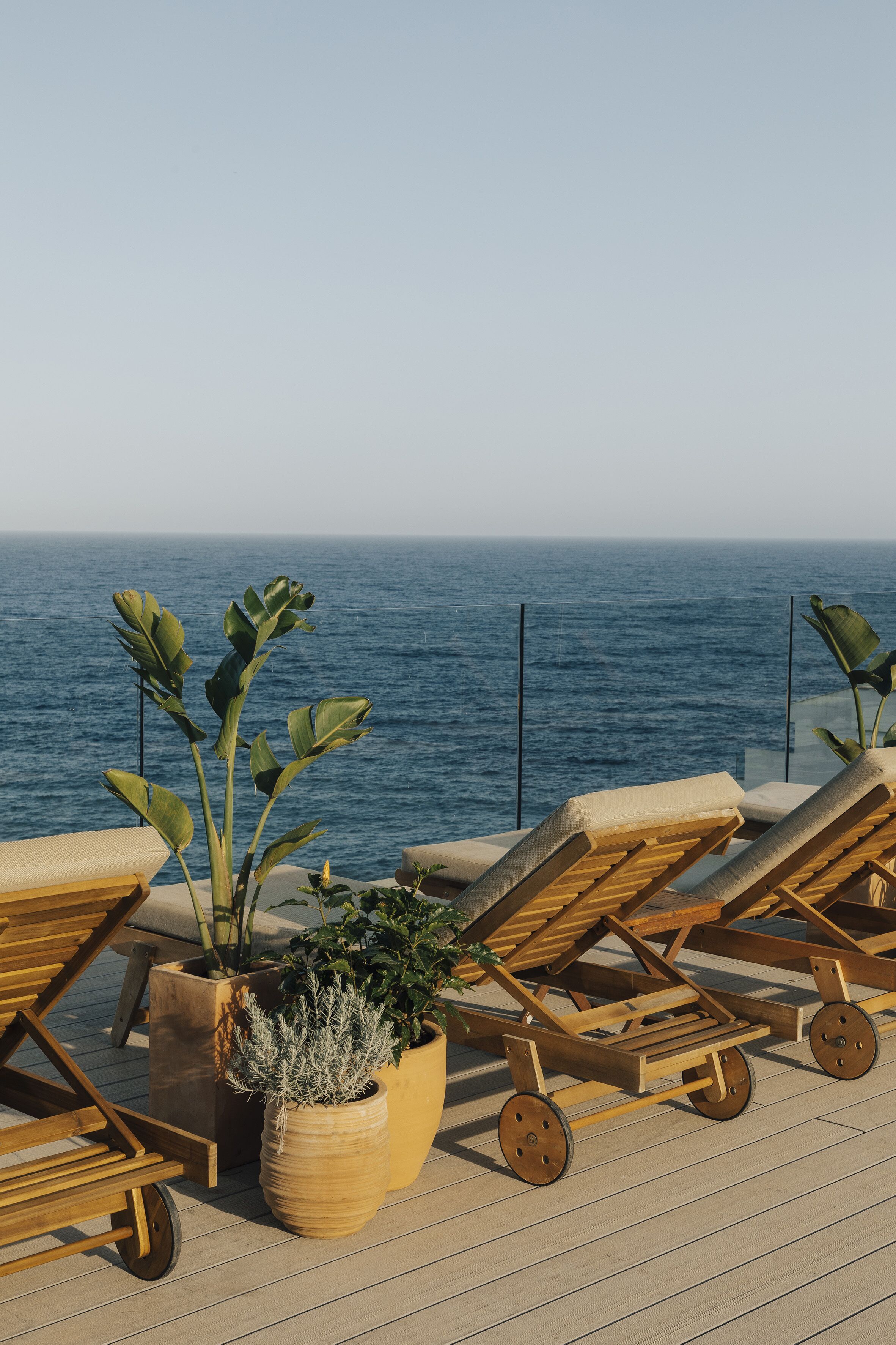 A deck with lounge chairs and potted plants overlooking the ocean.