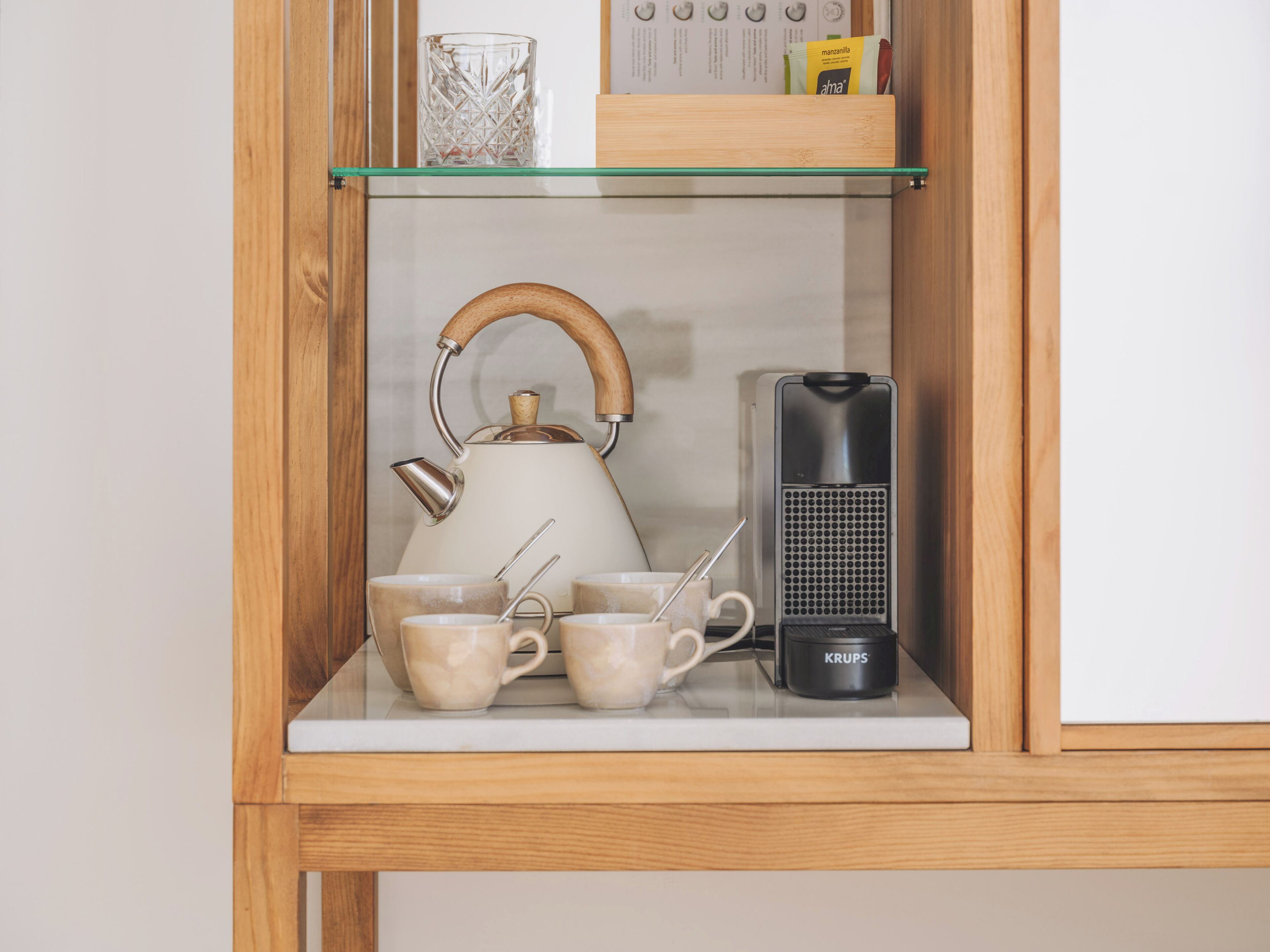 A shelf with a white kettle, cups, and a Krups electric kettle.