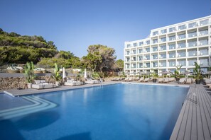 A swimming pool with lounge chairs and umbrellas, surrounded by a building with multiple balconies. - Meliá Ibiza  - Adults Only (Santa Eulalia del Rio)