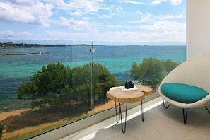 Uma varanda com vista para o mar, uma cadeira com almofada e uma mesa pequena com uma câmera.