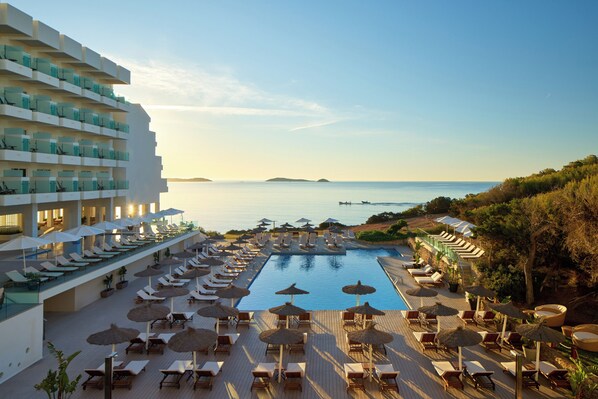 A resort pool area with sun loungers and umbrellas, overlooking a calm sea. - Meliá Ibiza  - Adults Only (Santa Eulalia del Rio)