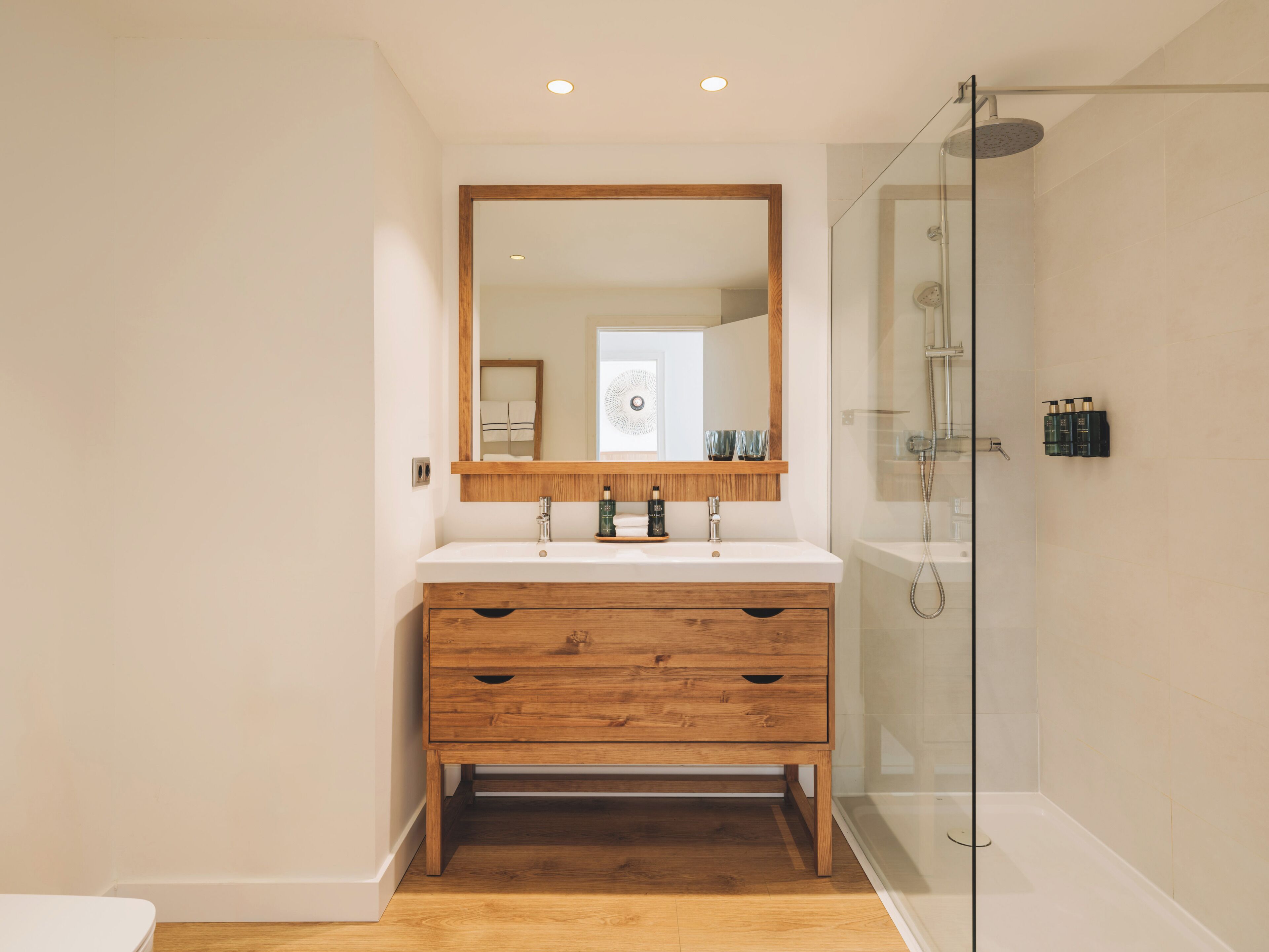 A modern bathroom with a wooden vanity, a large mirror, and a glass shower enclosure.
