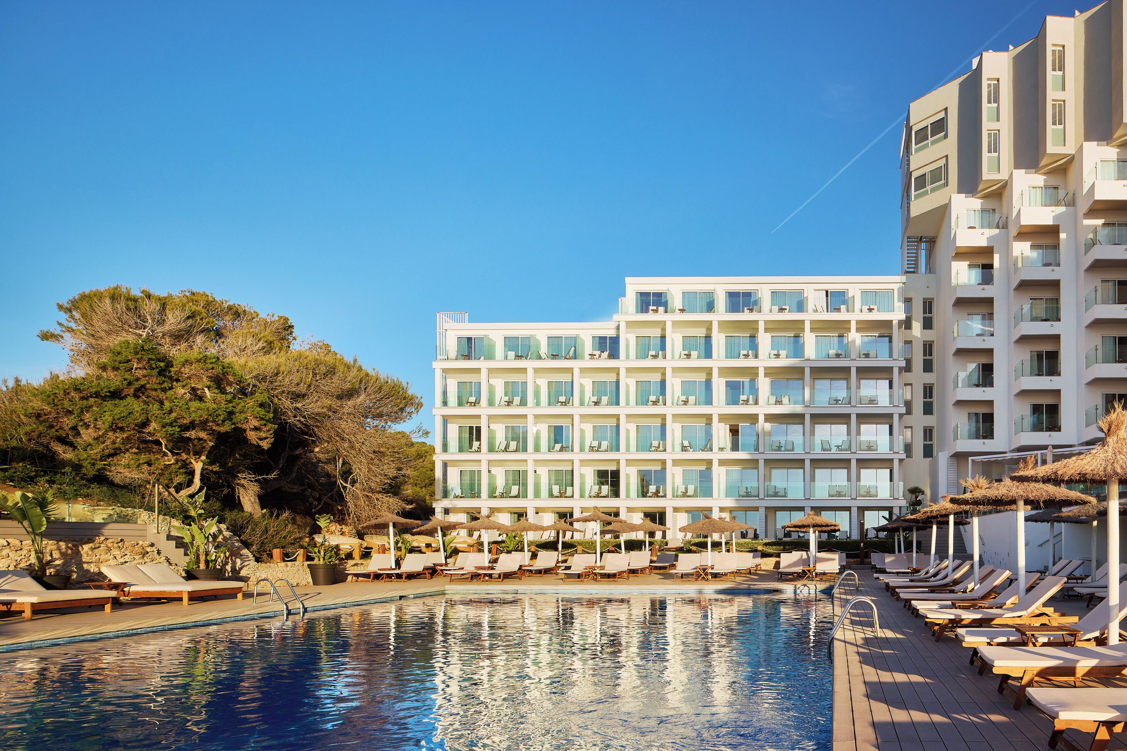 A hotel with a swimming pool, sun loungers, and a large building with multiple balconies.