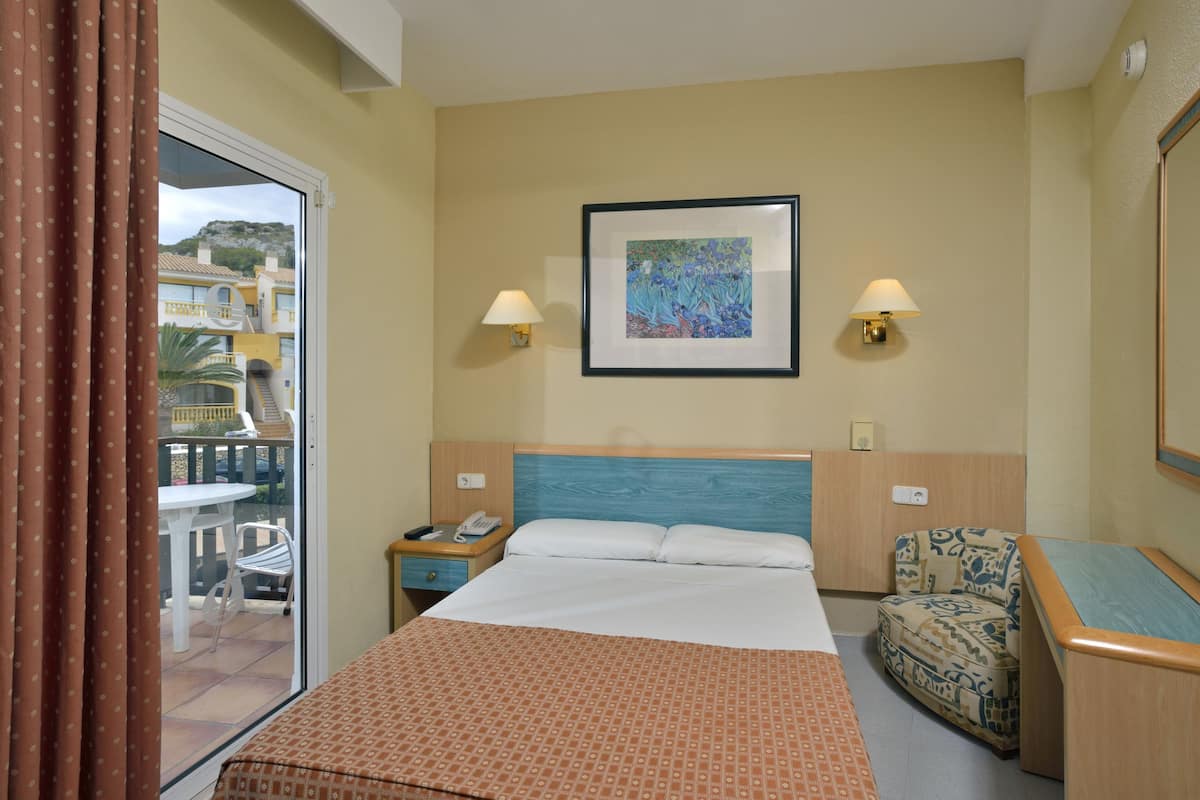 Ein Hotelzimmer mit Bett, Stuhl, Nachttisch und einem Fenster mit Vorhängen.