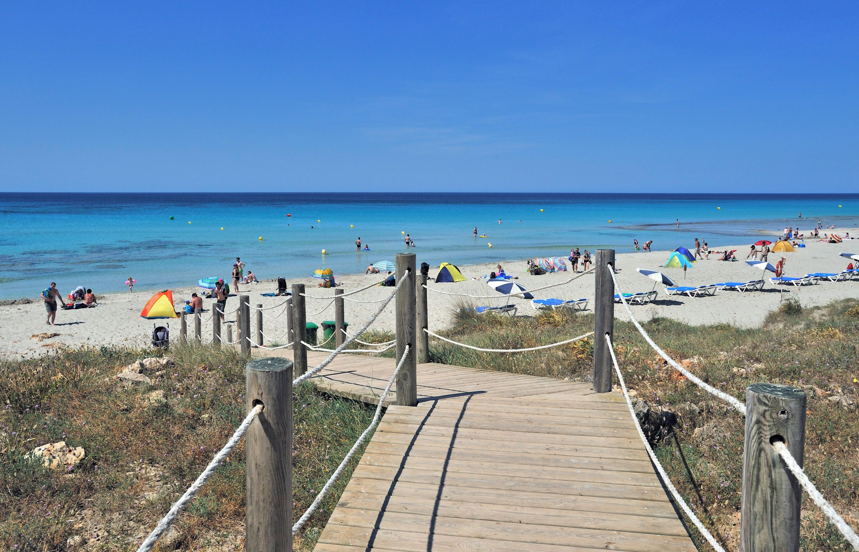 Een houten looppad dat naar een strand leidt, met parasols en strandstoelen.