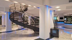 A modern hotel lobby with a curved staircase, marble flooring, and a reception desk. - Sol Milanos Pingüinos (Alayor)