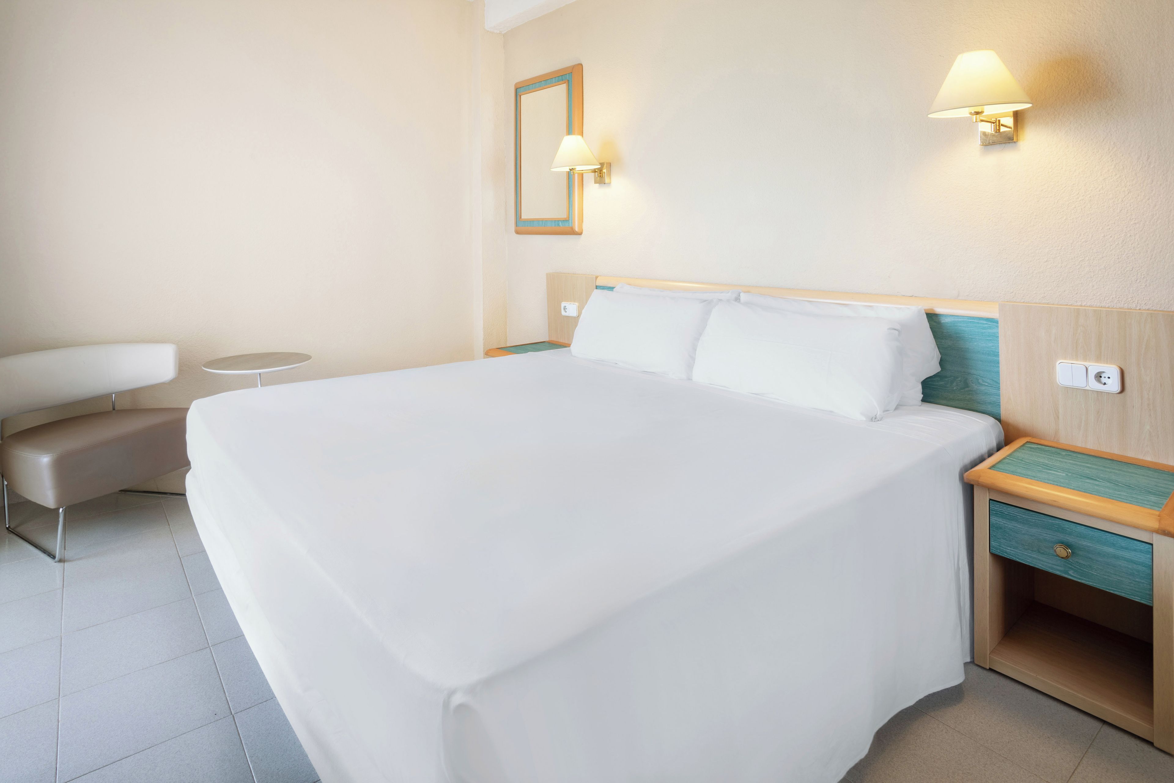 Ein Hotelzimmer mit einem großen Bett, Nachttischen, einem Sessel und einem Spiegel an der Wand.