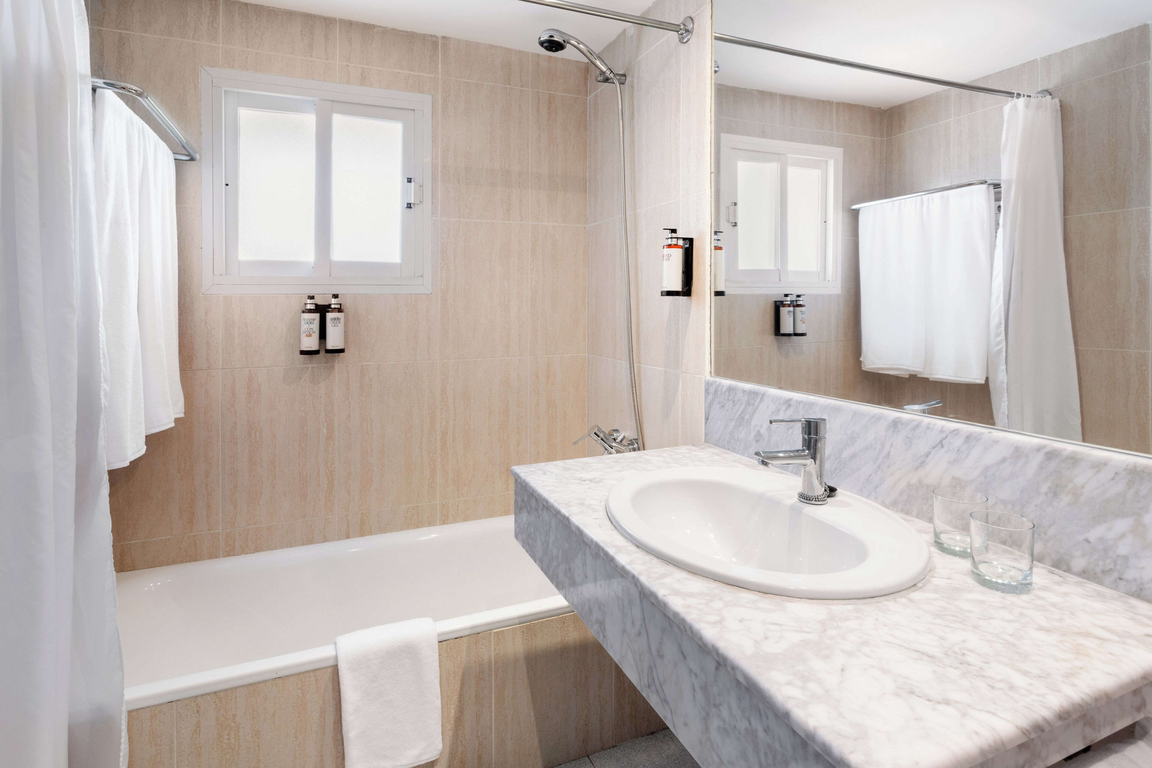 Une salle de bain moderne avec une baignoire, un lavabo doté d’un plan de toilette en marbre et un grand miroir.