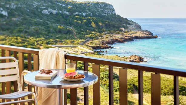 A balcony with a table set for breakfast, overlooking a coastal landscape with cliffs and the sea. - Sol Milanos Pingüinos (Alayor)