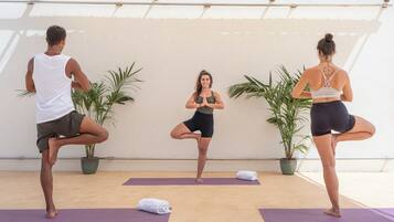 Tres personas practicando yoga sobre esterillas en una habitación con plantas en macetas y una pared blanca.