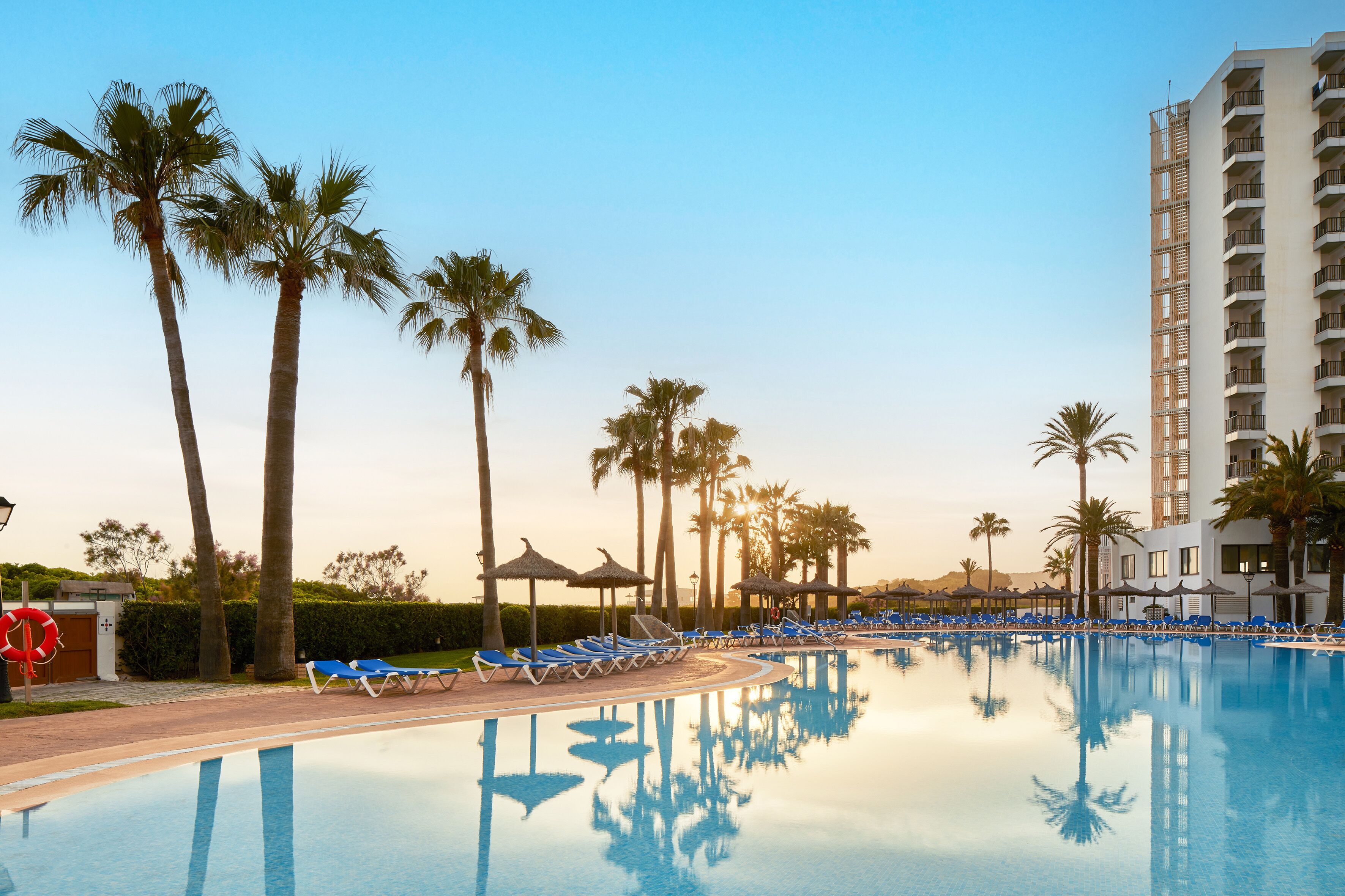 Un área de piscina con sillones de descanso y palmeras.