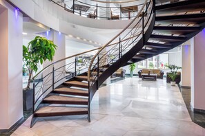 Un interior moderno con una escalera espiral, suelo de mármol y plantas de interior.