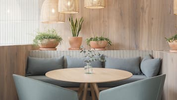 Un espacio de descanso moderno con una mesa redonda, sillas acolchadas y lámparas de mimbre colgantes.
