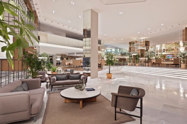 A spacious lobby with a high ceiling, multiple seating areas, and a large central column.