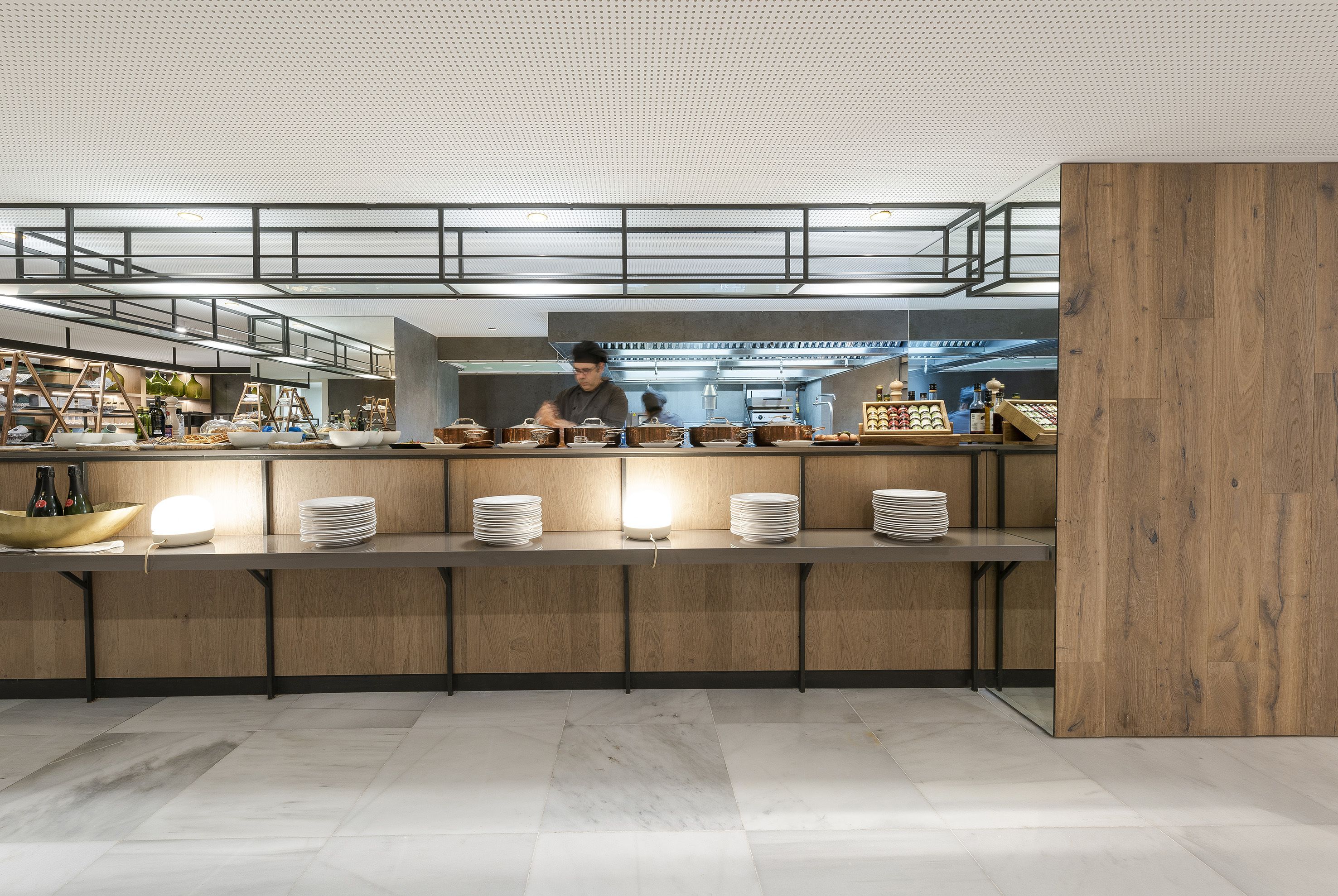 A modern kitchen with a chef preparing food, wooden countertops, and a bright overhead lighting system.