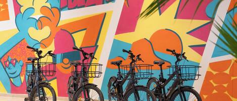 Four bicycles with baskets, parked against a colorful mural with the word "IBIZA" prominently displayed.