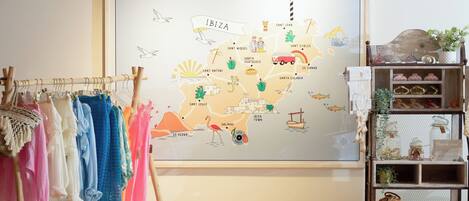 A map of Ibiza with labeled towns and attractions, a rack of colorful clothes, and a shelf with decorative items.