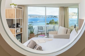 Ein Hotelzimmer mit Bett, einer Sitzecke mit Meerblick, einem Bücherregal und einem kleinen Tisch.