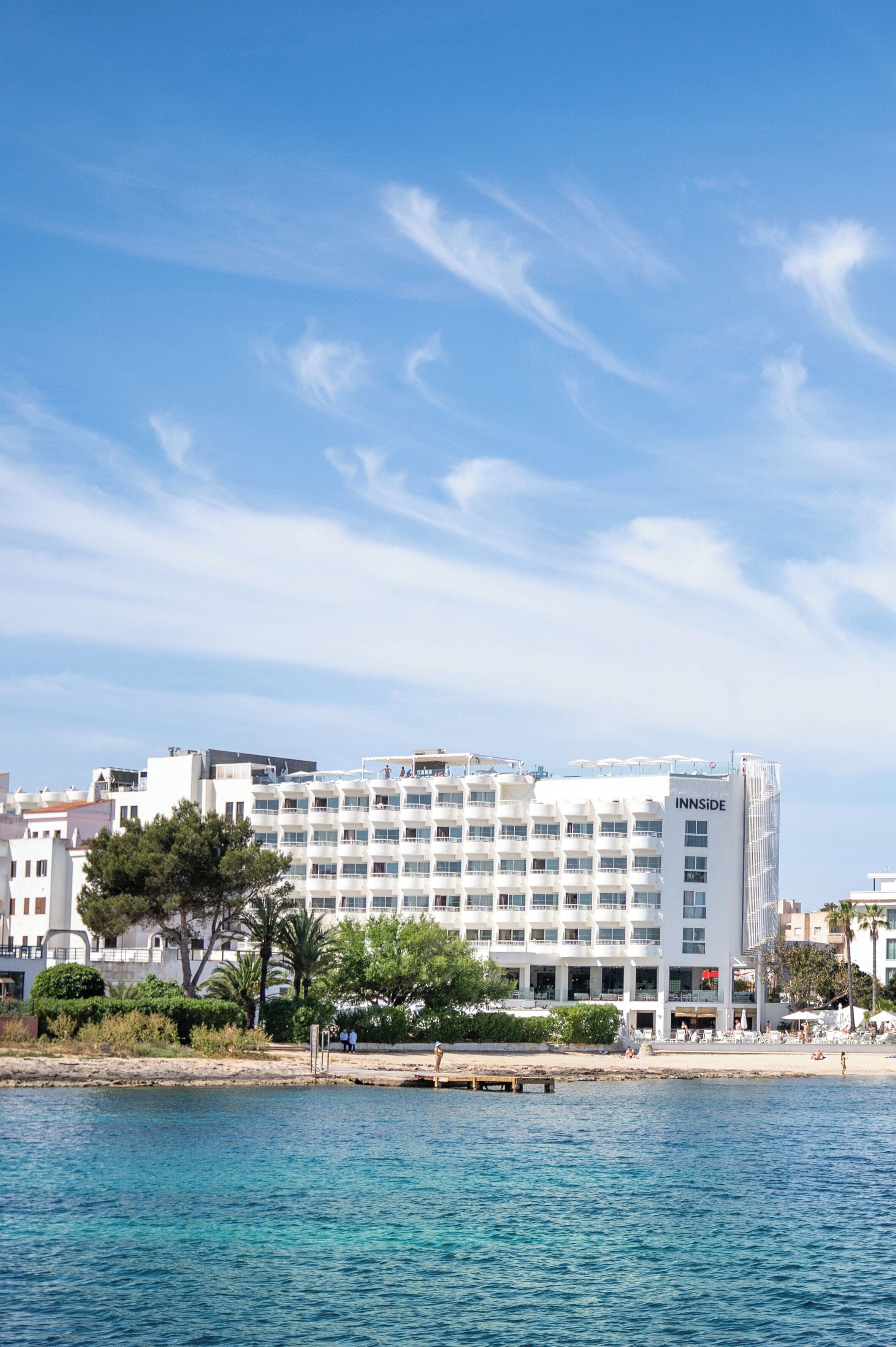 A multi-story hotel with balconies, located near a body of water.