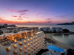 A resort with multiple balconies, a pool, and a view of the sea at sunset.