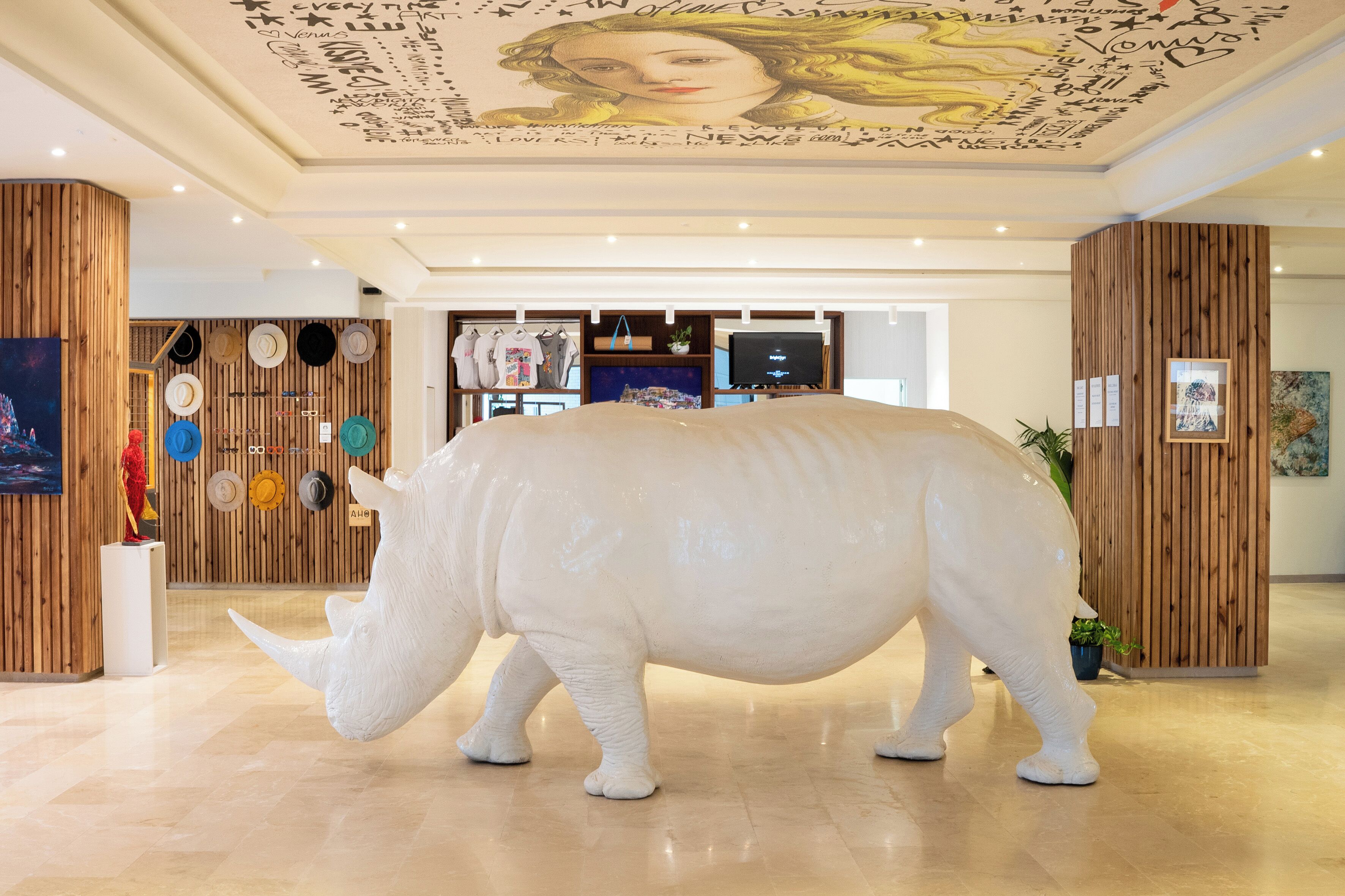 Una estatua grande de rinoceronte blanco en un vestíbulo con paneles de madera y un mural en el techo.