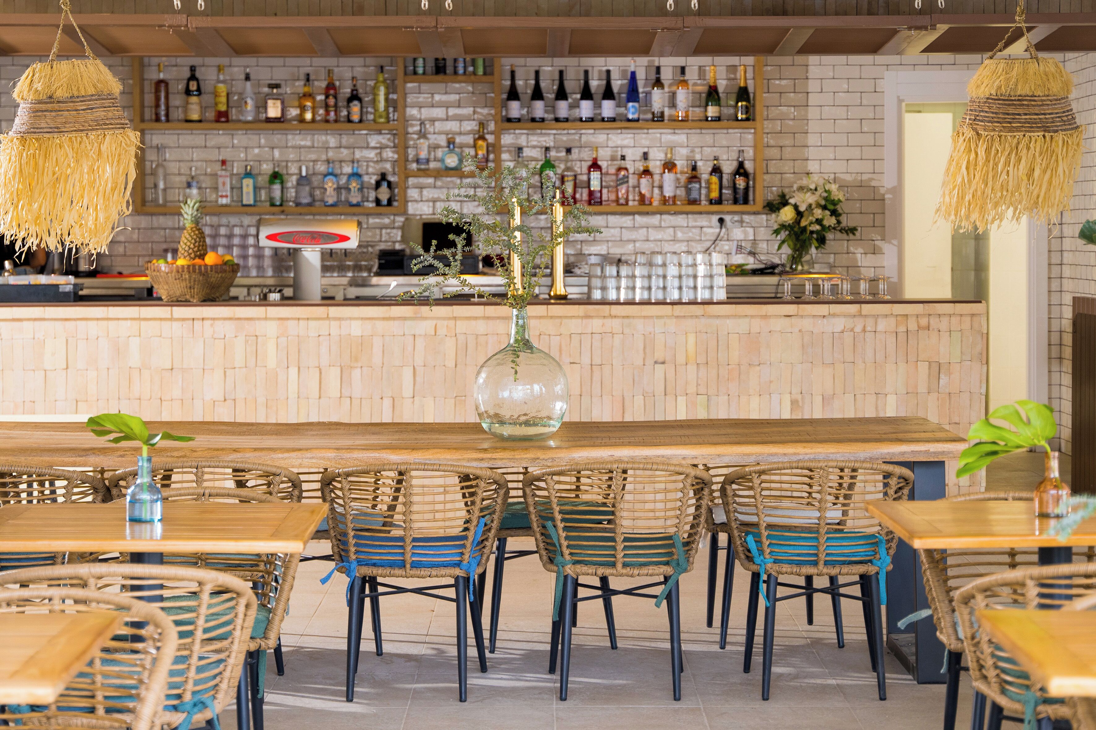 Un espace bar avec des chaises en osier, un comptoir central et des étagères remplies de bouteilles.