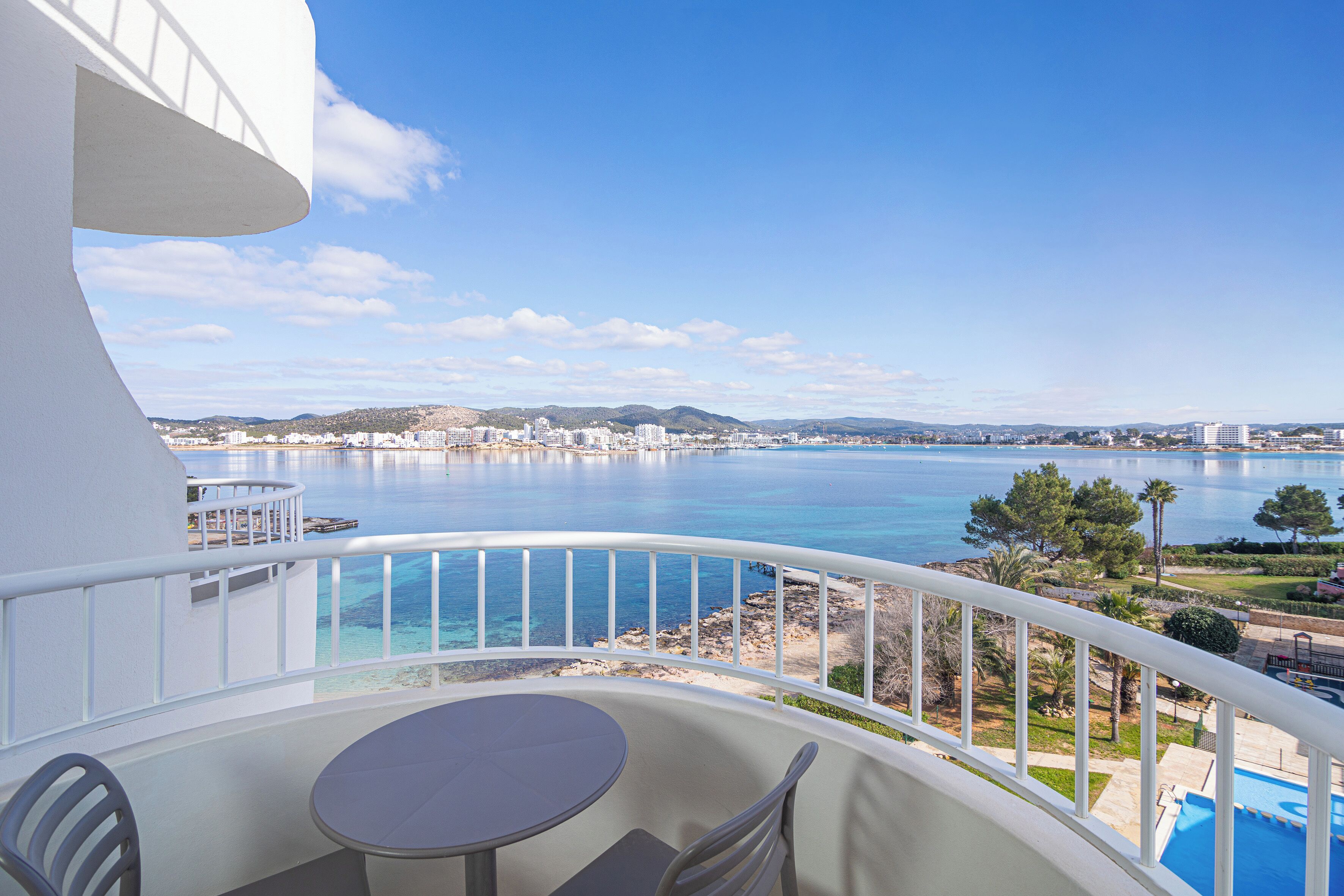 Un balcon avec une table et des chaises, offrant une vue sur un paysage urbain côtier et une mer bleue et limpide.