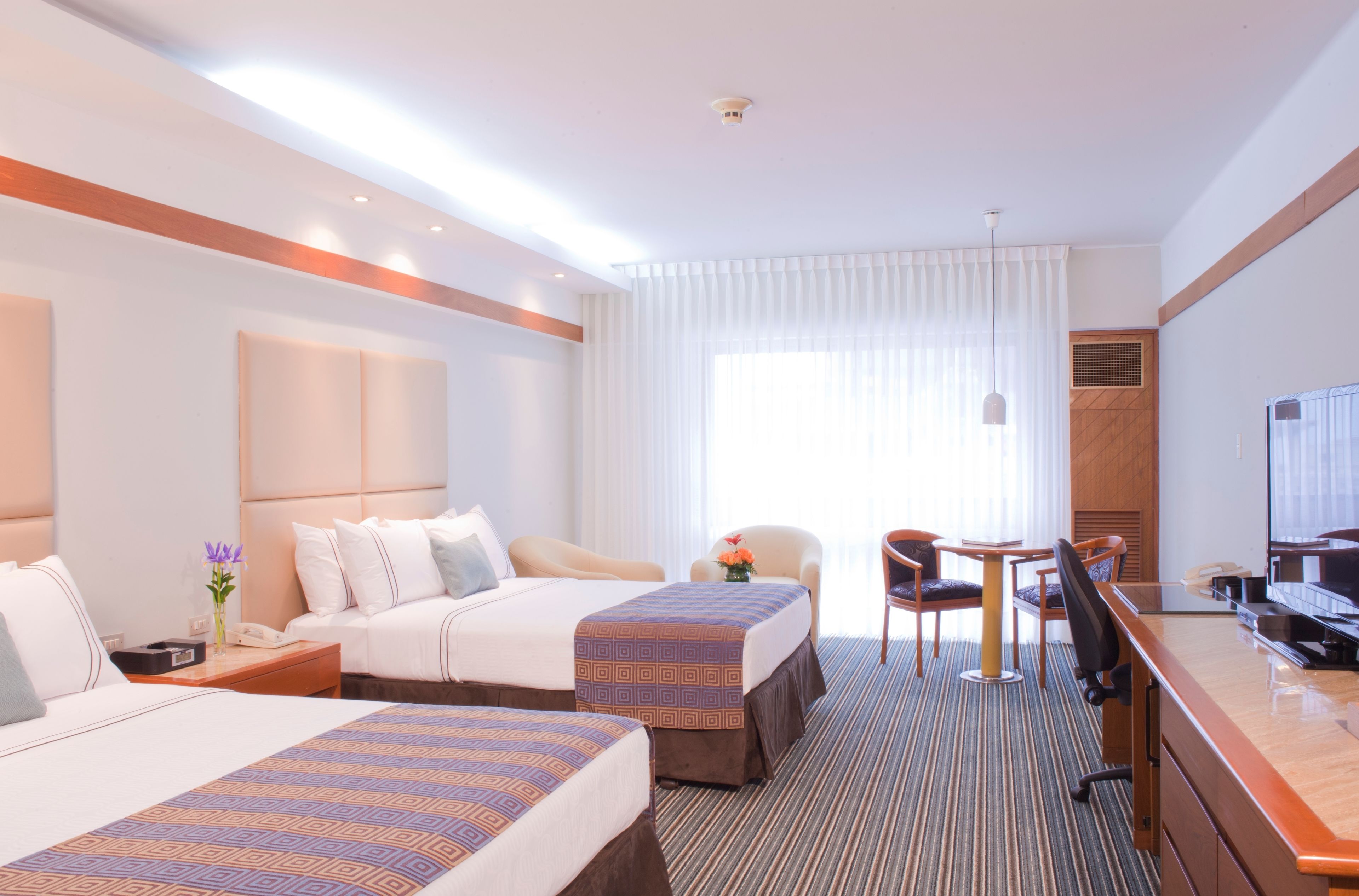 Una habitación de hotel con dos camas, un escritorio, una silla, un televisor y una ventana con cortinas.