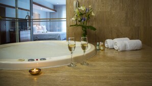 Un baño con una bañera, dos copas de vino blanco, una vela, un florero con flores y toallas sobre una encimera de madera.