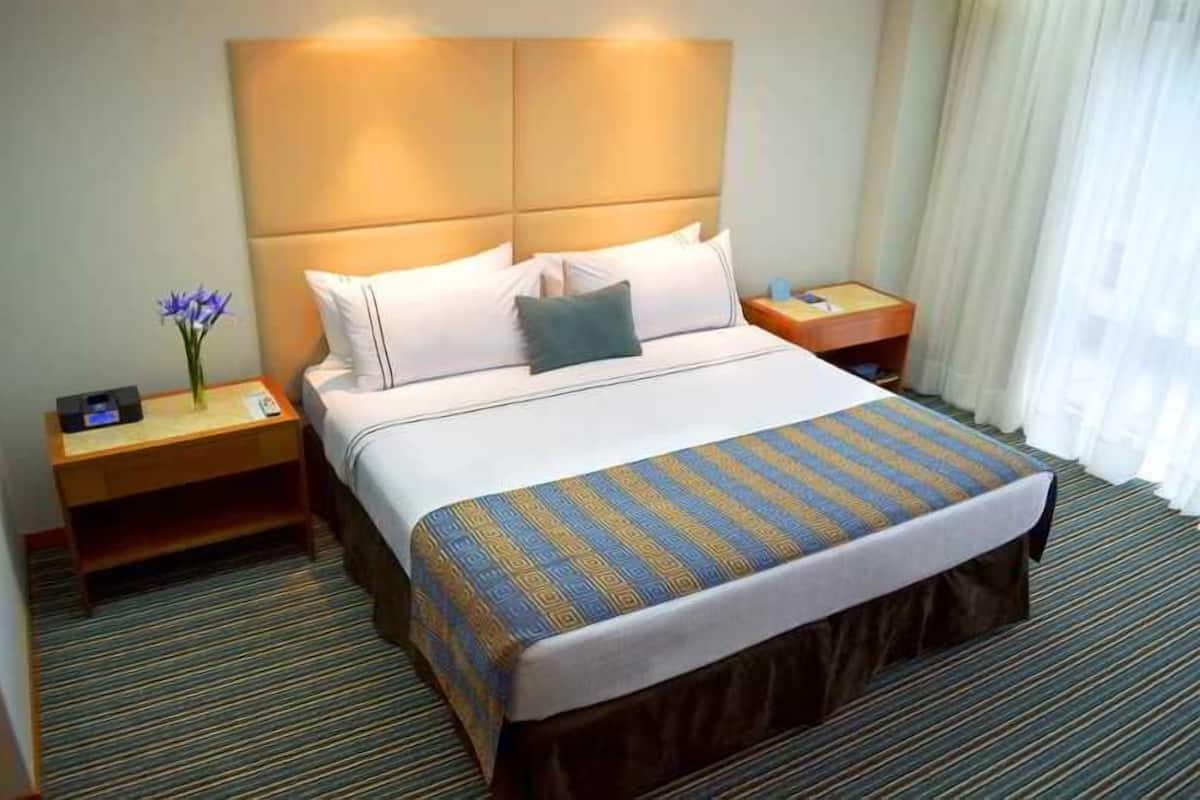 Ein Hotelzimmer mit einem großen Bett, einem Nachttisch, einer Lampe und einer Vase mit Blumen.