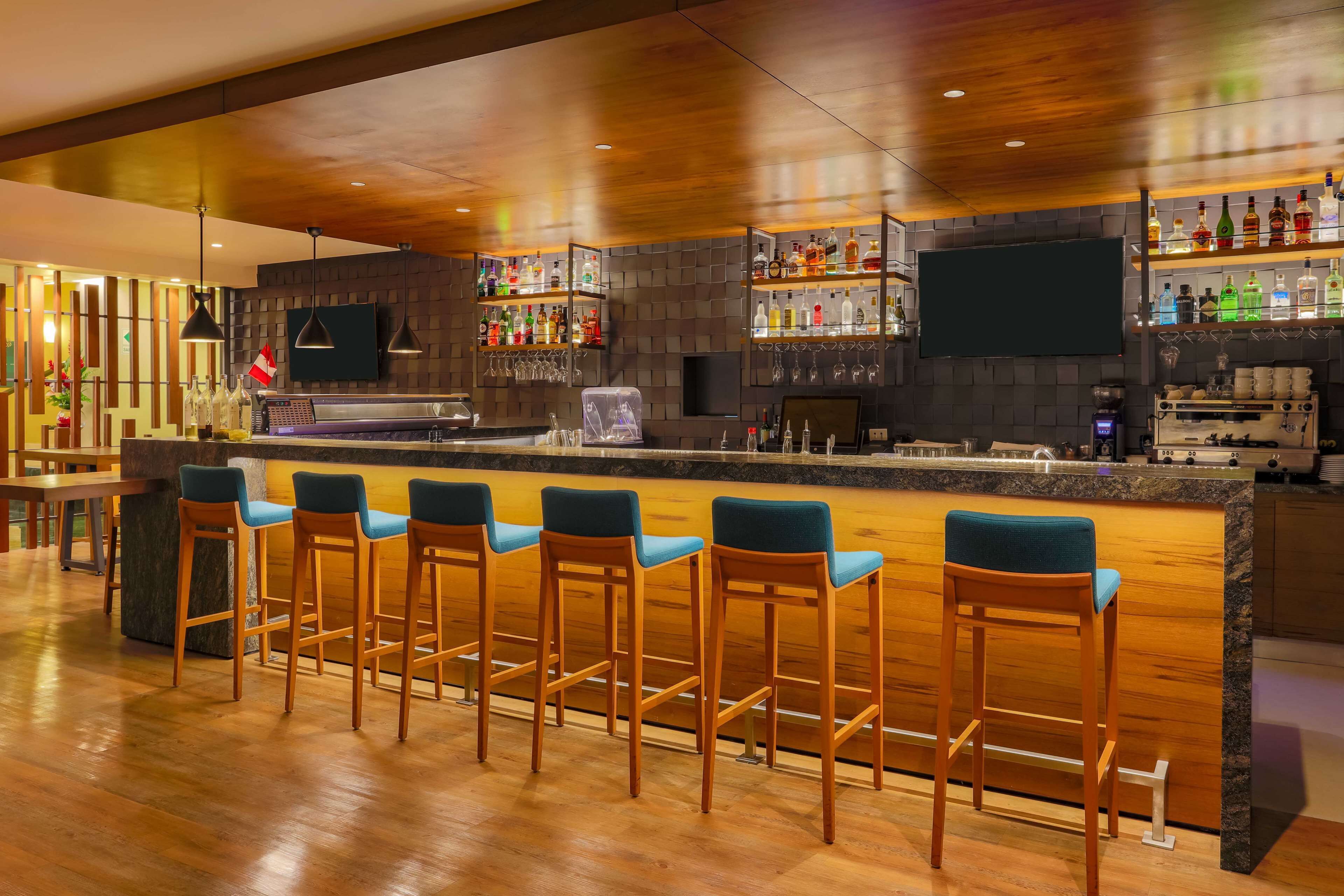 A bar area with a long counter, multiple stools, and shelves stocked with bottles.