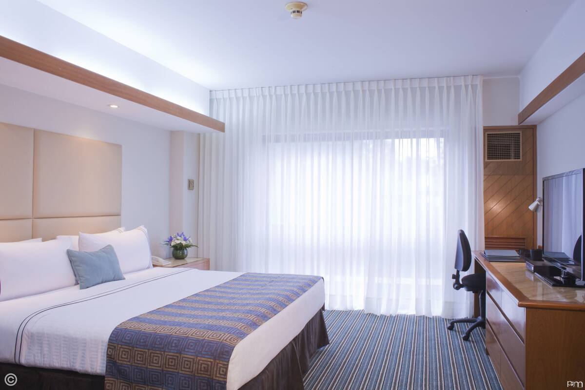 Quarto de hotel com uma cama grande, uma escrivaninha, uma cadeira e uma televisão.